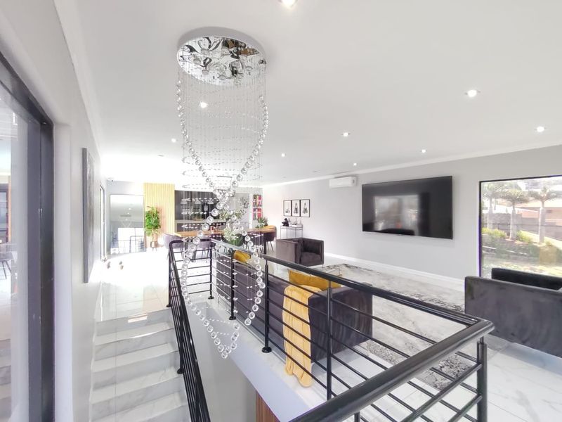 Spacious open-plan living area featuring modern marble-look flooring, a striking crystal chandelier, and a sleek metal staircase balustrade.