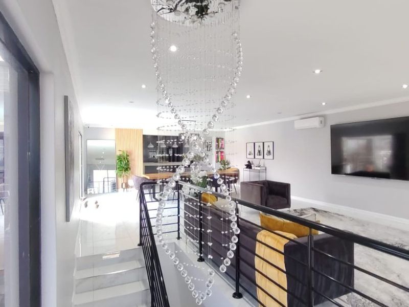 Spacious open-plan living area featuring a modern staircase with metal balustrade, recessed lighting, and sleek tiled flooring in a contemporary setting.