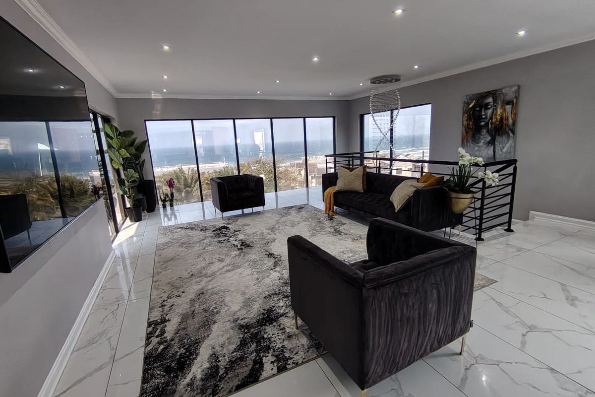 Modern open-plan living area featuring large floor-to-ceiling windows with ocean views, polished marble-look floor tiles, and contemporary recessed lighting.
