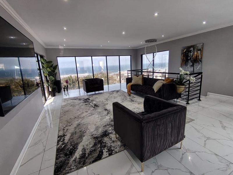 Modern open-plan living area featuring large floor-to-ceiling windows with ocean views, polished marble-look floor tiles, and contemporary recessed lighting.