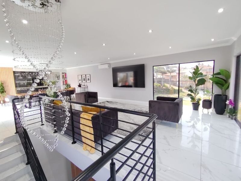 Spacious open-plan living area featuring polished porcelain tiles, modern recessed lighting, a striking crystal chandelier, and a sleek metal balustrade overlooking the lower level.
