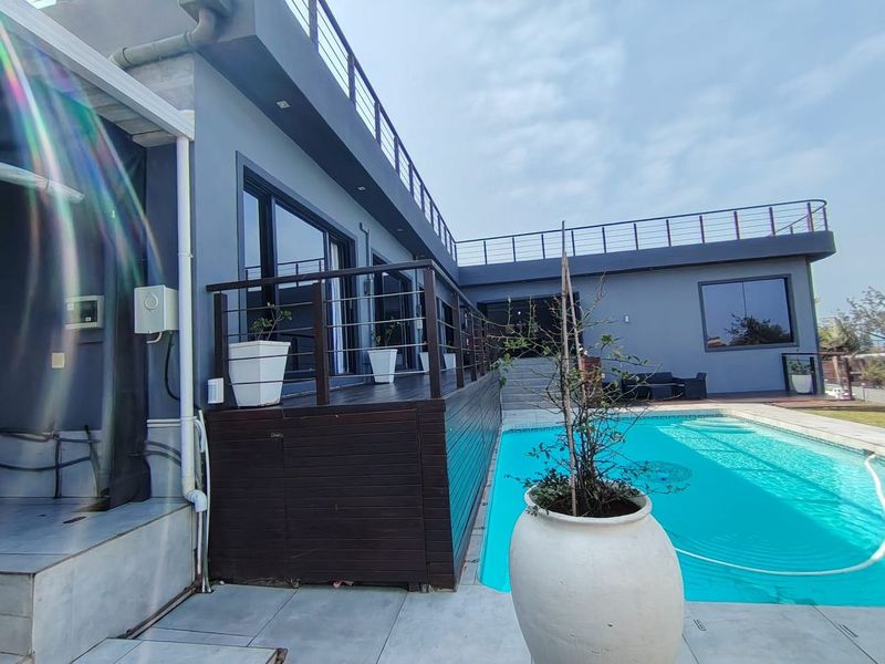 Modern outdoor pool area featuring timber decking, a sleek metal balustrade, and access to a spacious upper-level roof terrace.
