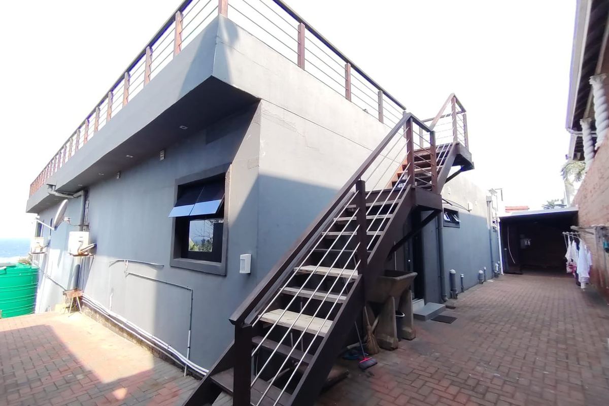 Rear exterior view featuring a paved courtyard, external staircase leading to a rooftop terrace, and modern grey rendered walls.