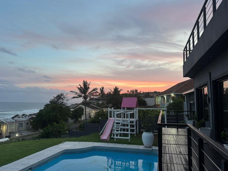 Outdoor pool area featuring timber decking, metal balustrades, and a swimming pool with scenic coastal sunset views.