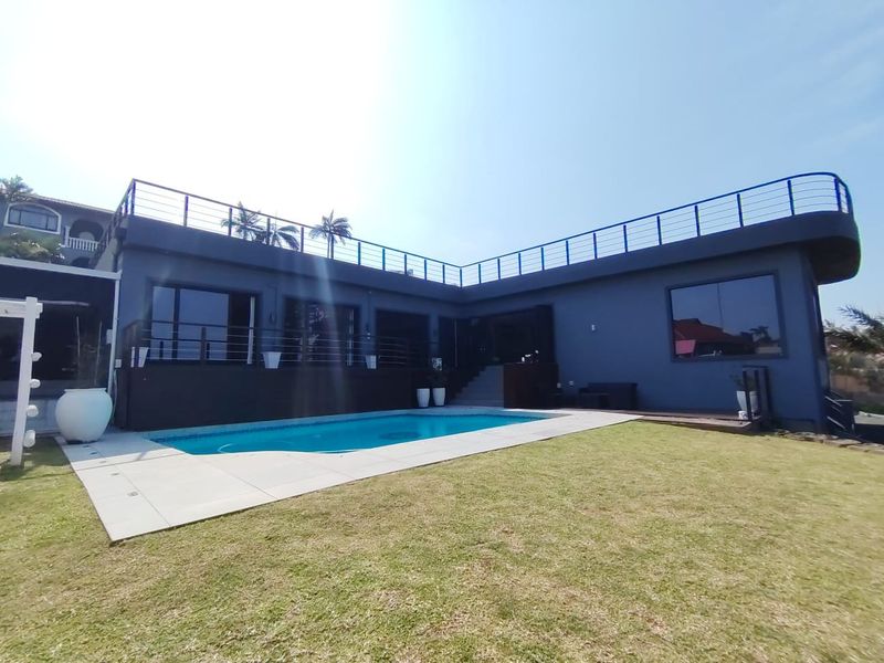 A well-maintained outdoor pool area featuring a swimming pool, paved surround, and a raised deck with safety railings.