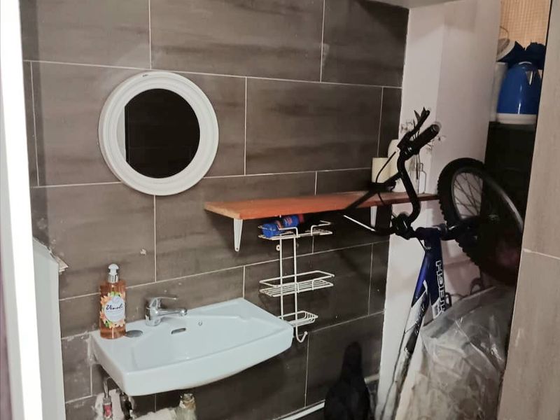 A small bathroom area featuring a wall-mounted basin, tiled walls, and overhead storage, currently used for utility storage.