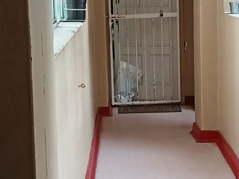 A narrow apartment hallway featuring tiled flooring, painted skirting boards, and a security gate at the end of the corridor.