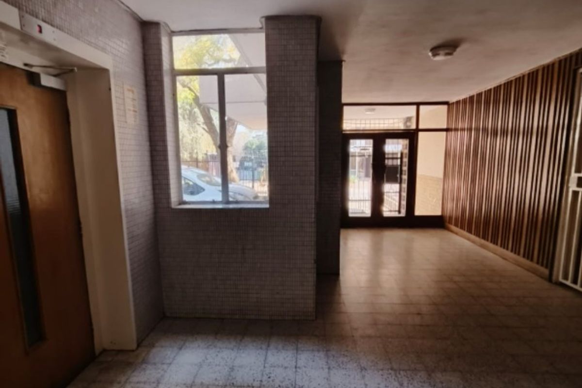 A spacious apartment building entrance lobby featuring tiled flooring, decorative timber wall paneling, and glass-paneled doors leading to the exterior.