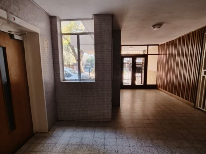 A spacious apartment building entrance lobby featuring tiled flooring, decorative timber wall paneling, and glass-paneled doors leading to the exterior.
