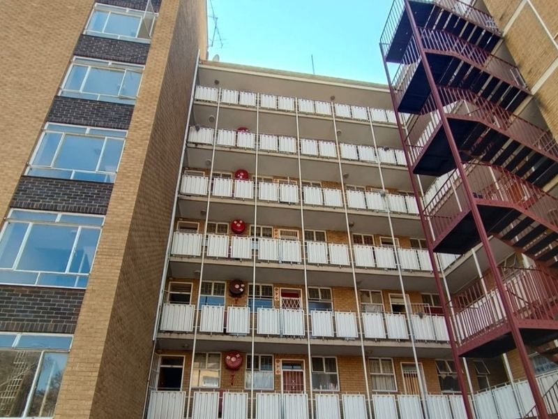 Rear elevation of a multi-story apartment building featuring external metal fire escape stairs and multiple levels of balconies with fire safety equipment.