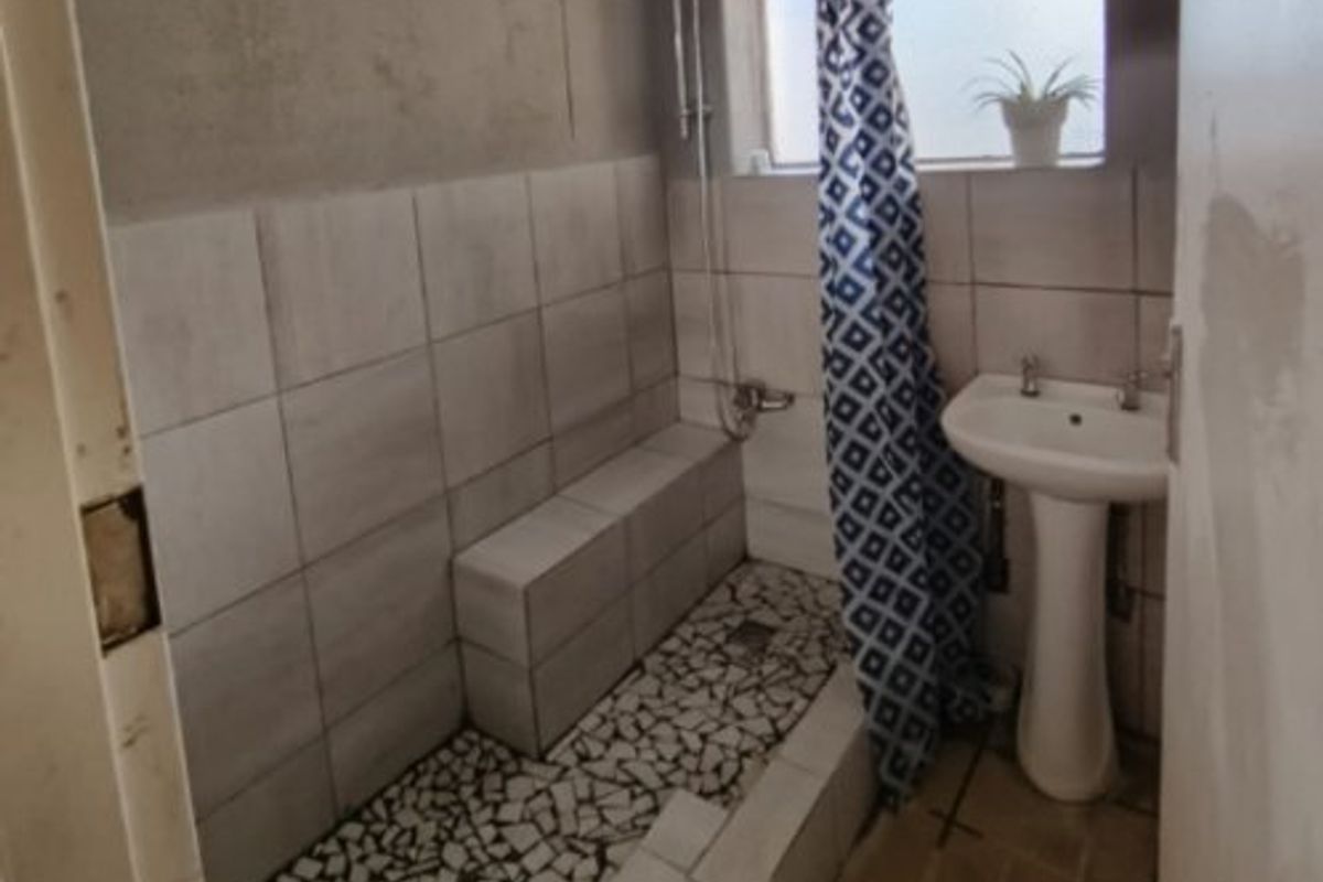 A compact bathroom featuring a pedestal basin and a tiled shower area with unfinished wall surfaces, requiring renovation to improve functionality and aesthetic appeal.