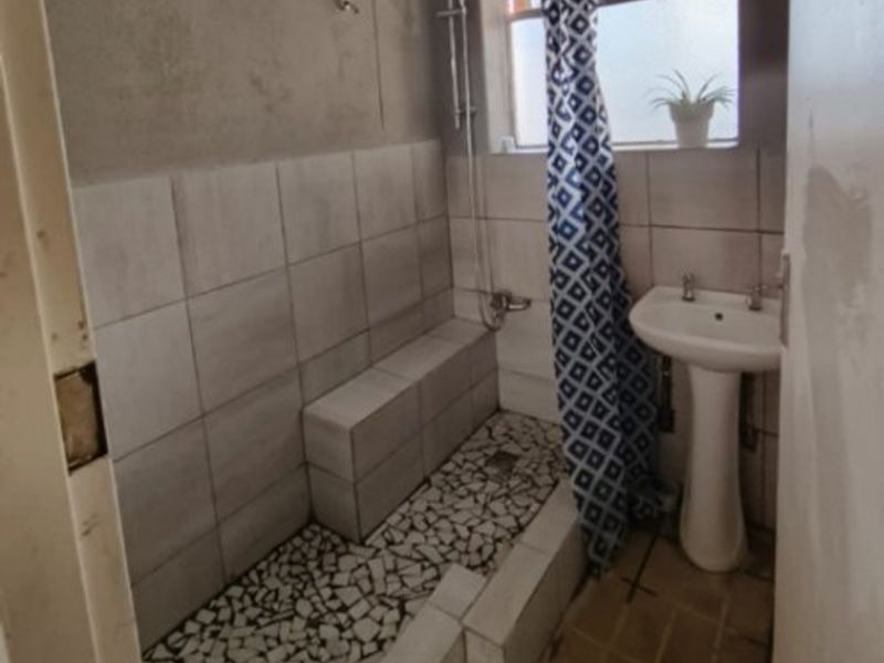 A compact bathroom featuring a pedestal basin and a tiled shower area with unfinished wall surfaces, requiring renovation to improve functionality and aesthetic appeal.
