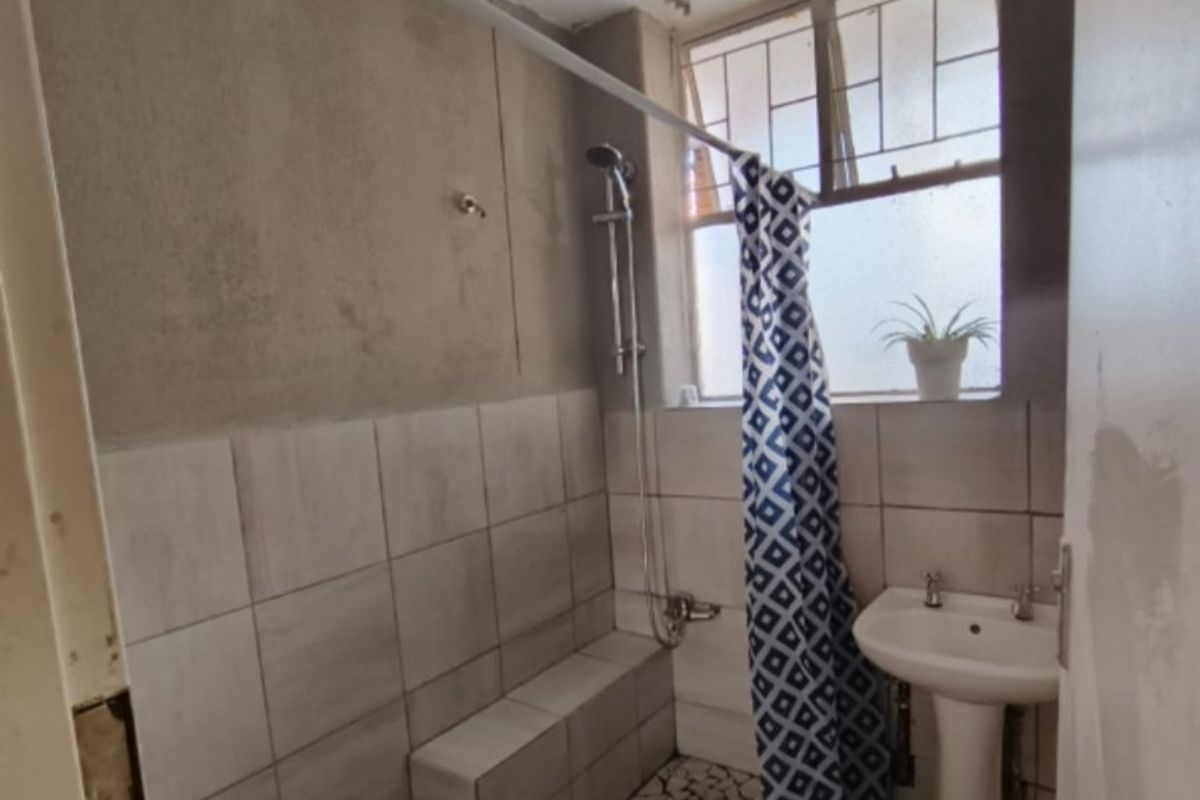 A compact bathroom featuring a pedestal basin and a tiled shower area with unfinished wall surfaces, requiring renovation to improve functionality and aesthetic appeal.