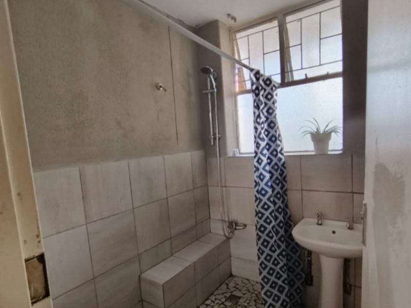 A compact bathroom featuring a pedestal basin and a tiled shower area with unfinished wall surfaces, requiring renovation to improve functionality and aesthetic appeal.
