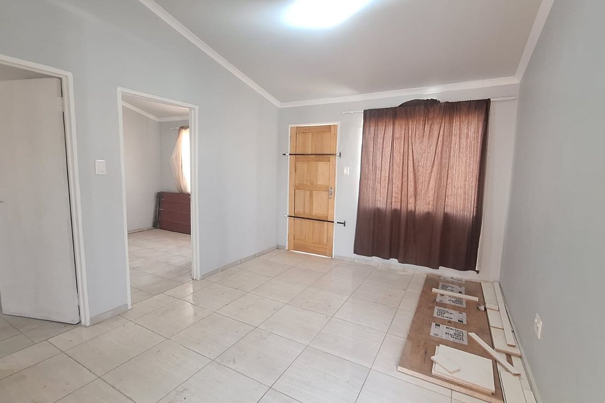 An empty living room featuring tiled flooring, coved cornicing, and a timber panel door, offering a blank canvas for interior design.