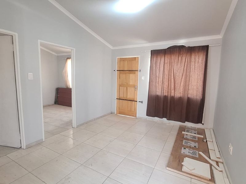An empty living room featuring tiled flooring, coved cornicing, and a timber panel door, offering a blank canvas for interior design.