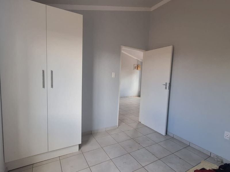 A clean, empty bedroom featuring neutral wall paint, tiled flooring, and a modern white built-in wardrobe.