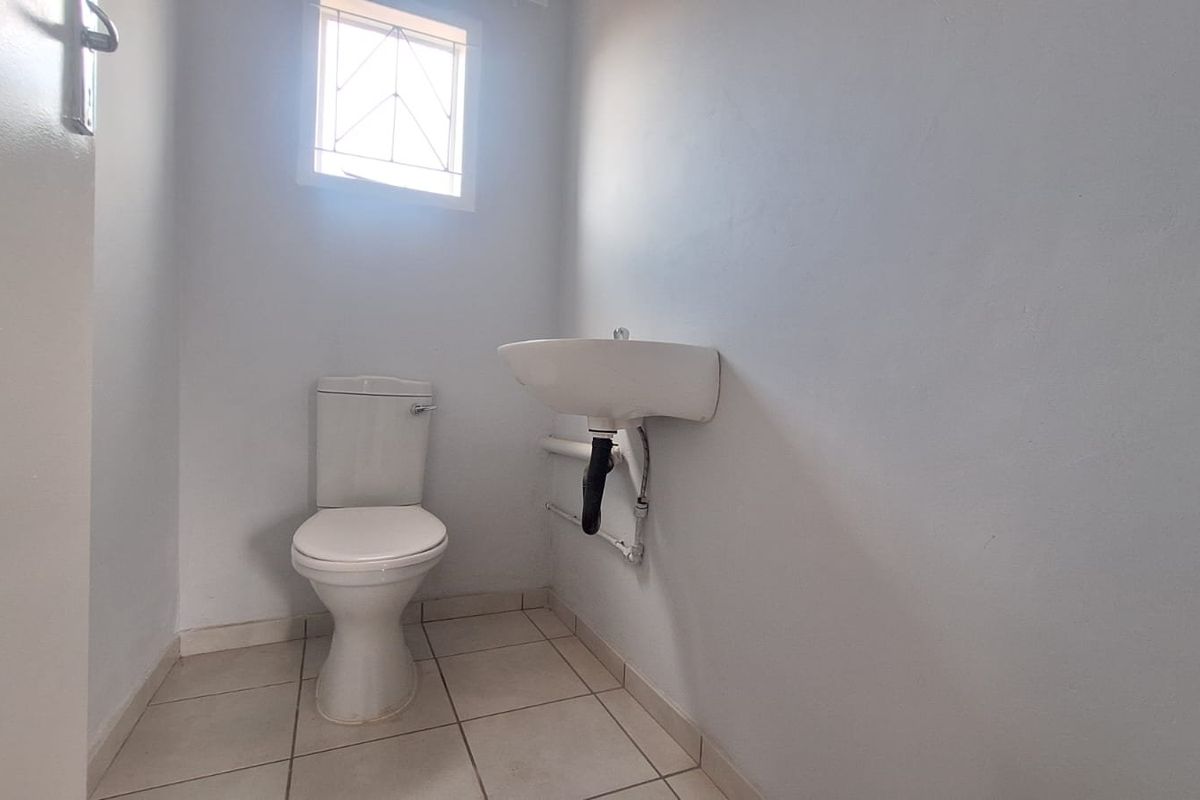 A simple, functional guest bathroom featuring a toilet, wall-mounted basin, and tiled flooring with a small window for natural light.