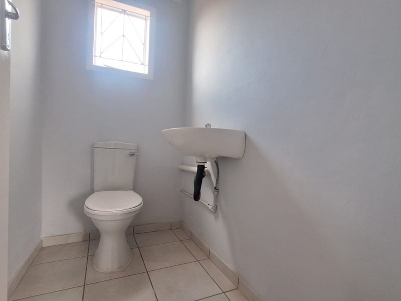 A simple, functional guest bathroom featuring a toilet, wall-mounted basin, and tiled flooring with a small window for natural light.