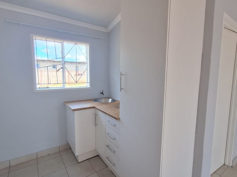 A clean and functional laundry area featuring built-in cabinetry, a stainless steel sink, tiled flooring, and a window with security bars.