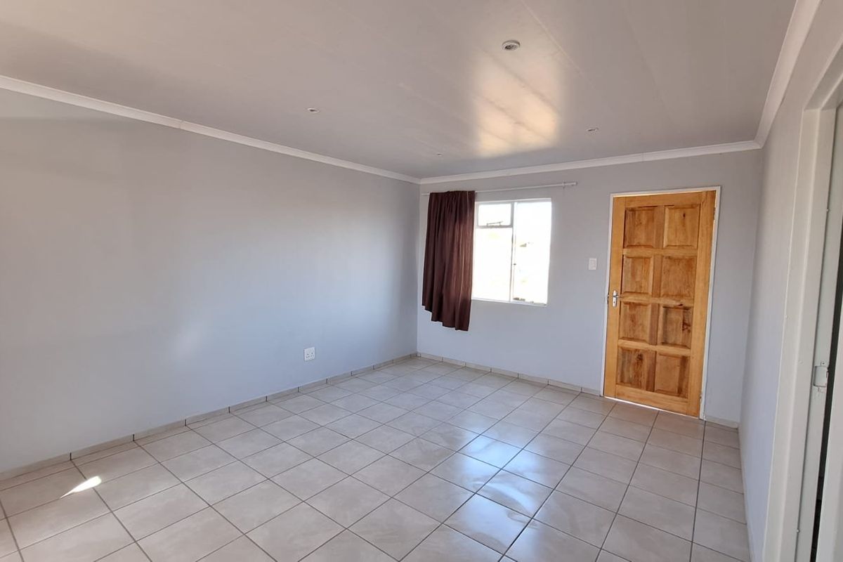 A bright, empty bedroom featuring neutral wall paint, tiled flooring, and a solid wooden door, offering a clean canvas for personalization.