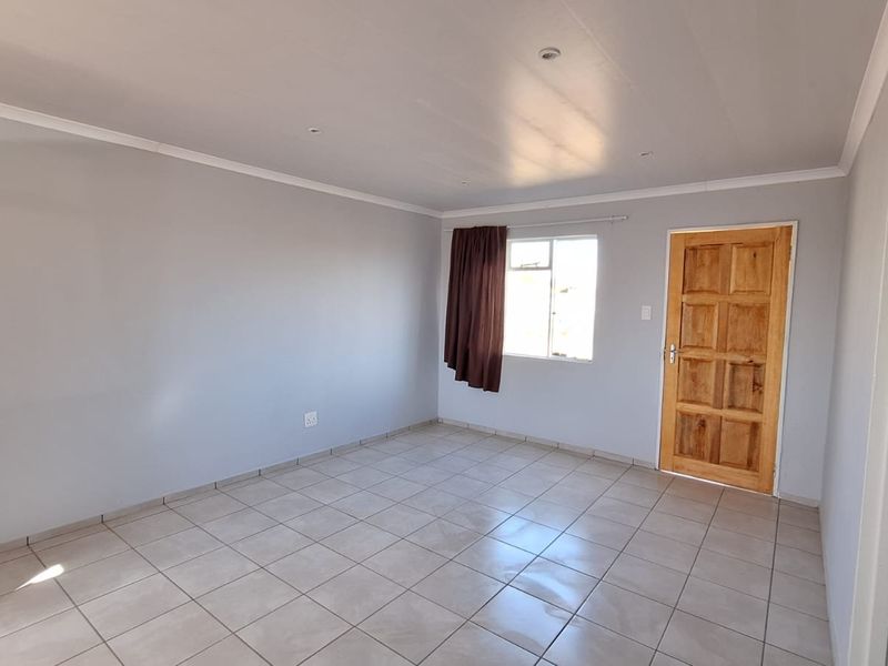 A bright, empty bedroom featuring neutral wall paint, tiled flooring, and a solid wooden door, offering a clean canvas for personalization.