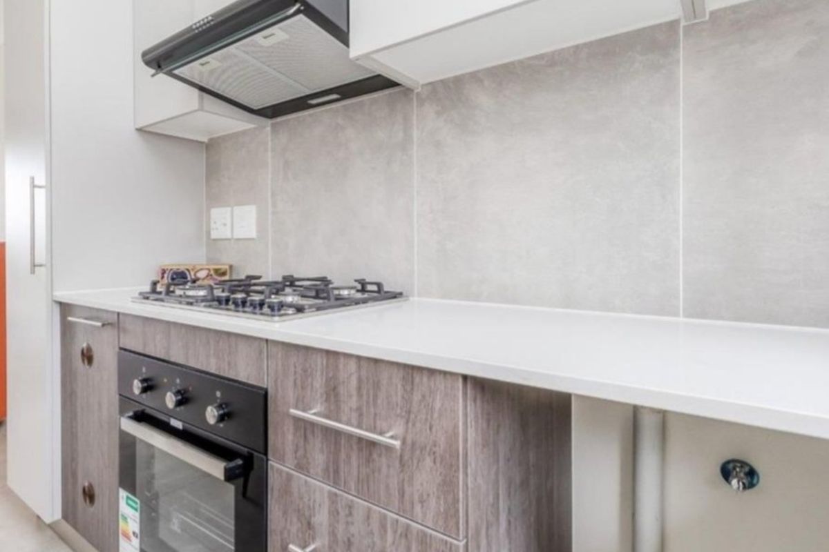 Modern kitchen featuring stone countertops, built-in gas cooktop, oven, extractor fan, and contemporary laminate cabinetry with a neutral tiled splashback.