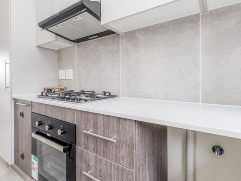 Modern kitchen featuring stone countertops, built-in gas cooktop, oven, extractor fan, and contemporary laminate cabinetry with a neutral tiled splashback.