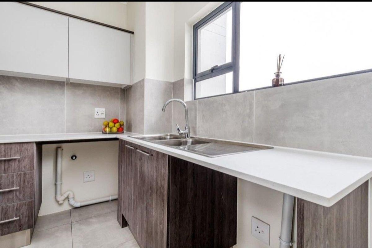 A modern kitchen featuring sleek cabinetry, stone countertops, a stainless steel sink, and neutral tiled finishes, offering a clean and functional workspace.