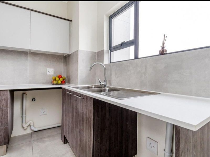 A modern kitchen featuring sleek cabinetry, stone countertops, a stainless steel sink, and neutral tiled finishes, offering a clean and functional workspace.
