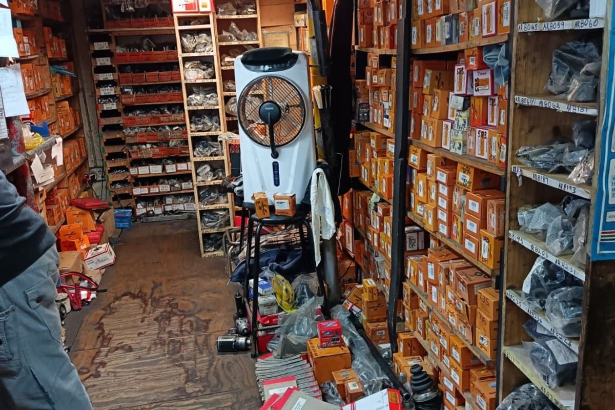A commercial utility storage space featuring extensive built-in timber shelving units filled with inventory and worn timber flooring.