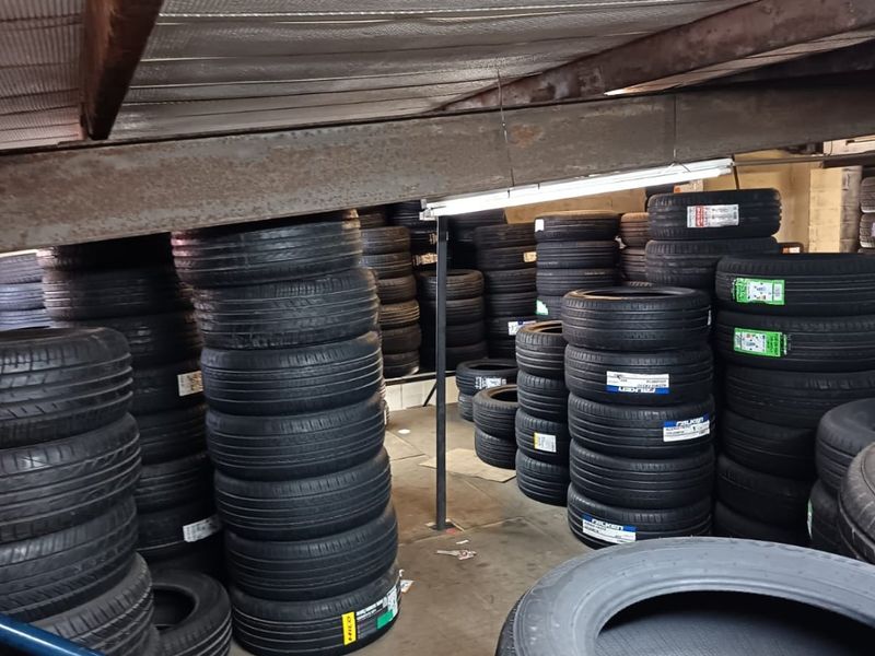 A commercial utility storage area featuring exposed structural beams, concrete flooring, and fluorescent lighting, currently utilized for tire inventory storage.