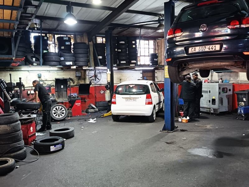Commercial automotive workshop featuring a vehicle lift, industrial steel roof structure, and dedicated tyre storage racking on a concrete floor.