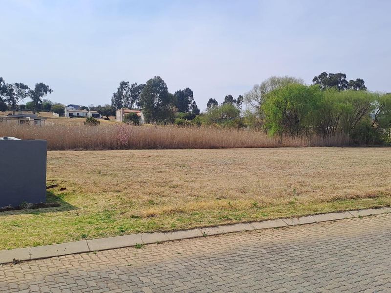 A vacant residential plot featuring a paved street frontage, concrete curbing, and a partial boundary wall, ready for development.
