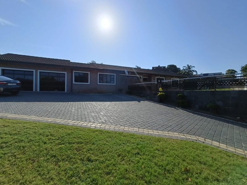 Front view of the property featuring a spacious paved driveway, double garage, and a well-maintained retaining wall with metal balustrades.