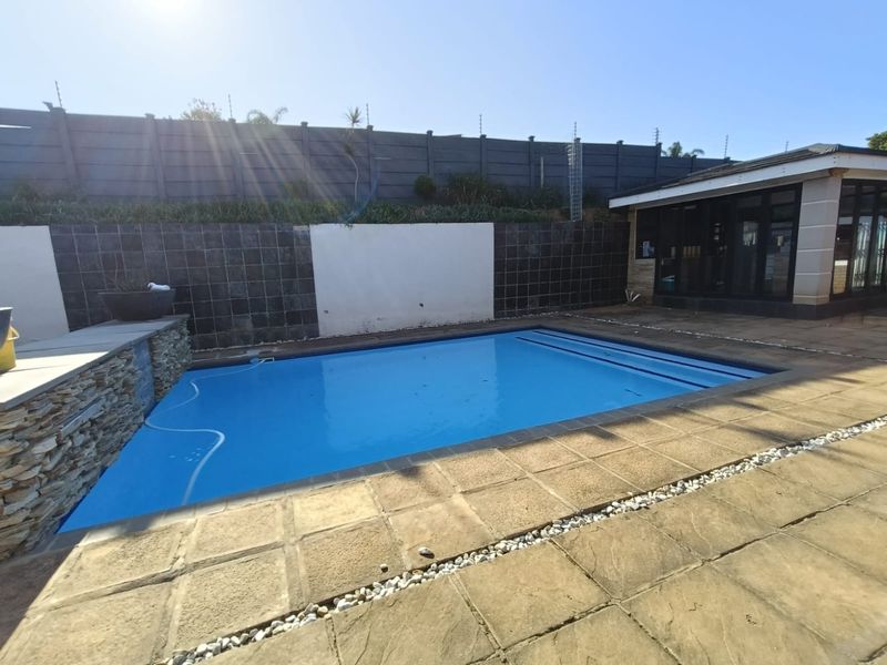 Outdoor pool area featuring a swimming pool with stone cladding accents, paved surround, and a secure boundary wall with electric fencing.