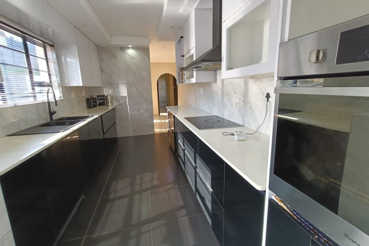 Modern galley-style kitchen featuring high-gloss cabinetry, stone countertops, integrated oven, electric hob, and elegant marble-look wall tiling with dark floor tiles.