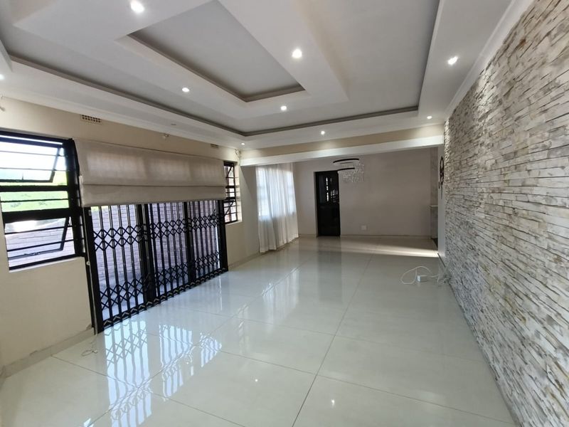 Spacious living area featuring a modern recessed ceiling with downlights, polished tiled flooring, and a decorative stone feature wall.