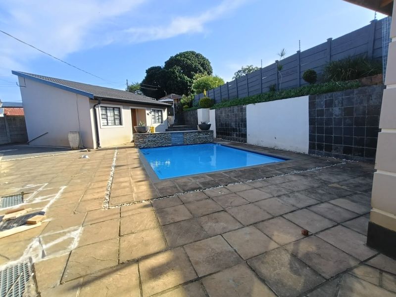 Outdoor pool area featuring a stone-clad water feature, paved patio surround, and secure perimeter walling with electric fencing.
