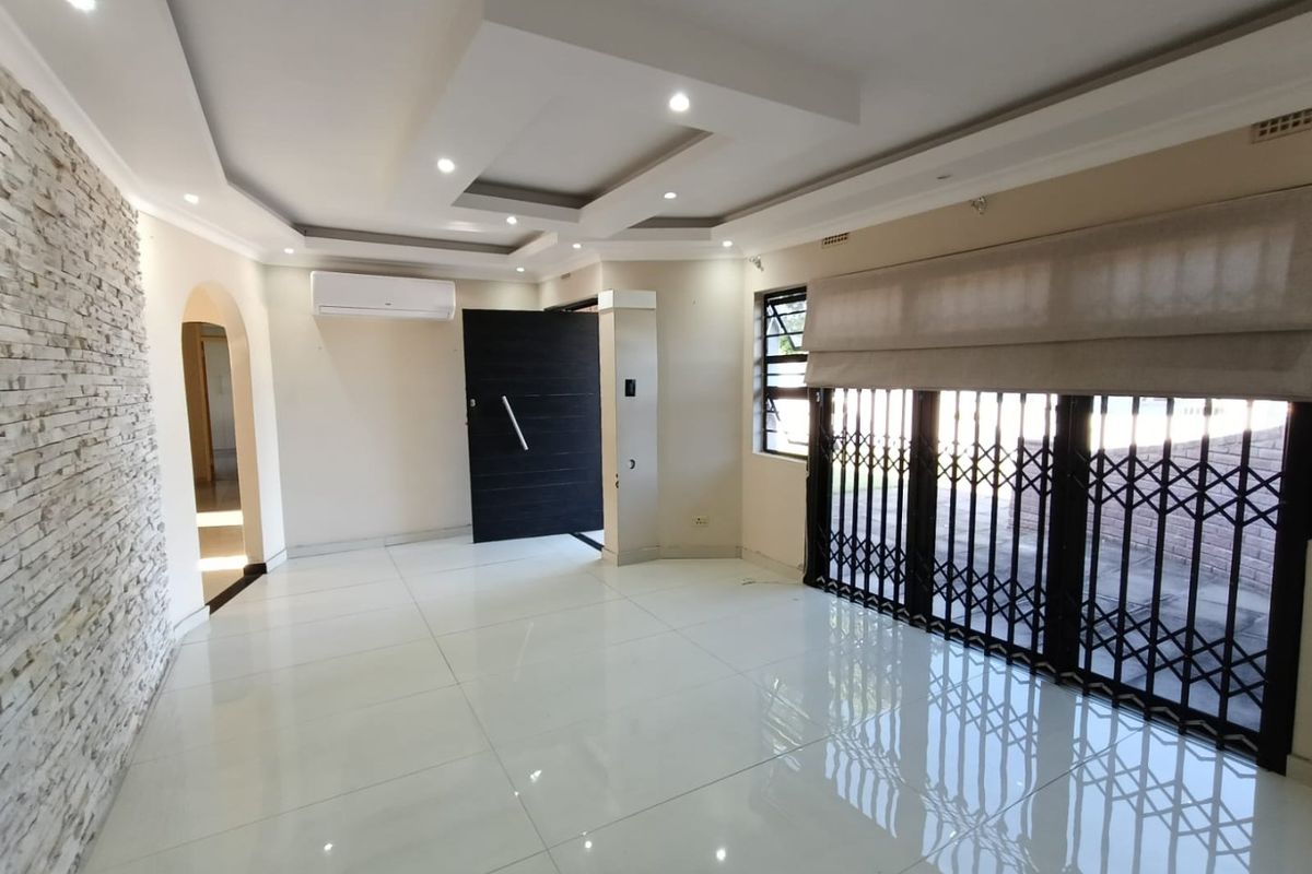 Spacious living area featuring polished porcelain tiles, a modern recessed ceiling with downlights, a stone feature wall, and a split-system air conditioner.