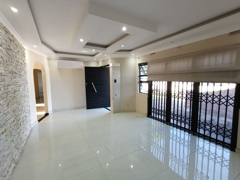 Spacious living area featuring polished porcelain tiles, a modern recessed ceiling with downlights, a stone feature wall, and a split-system air conditioner.