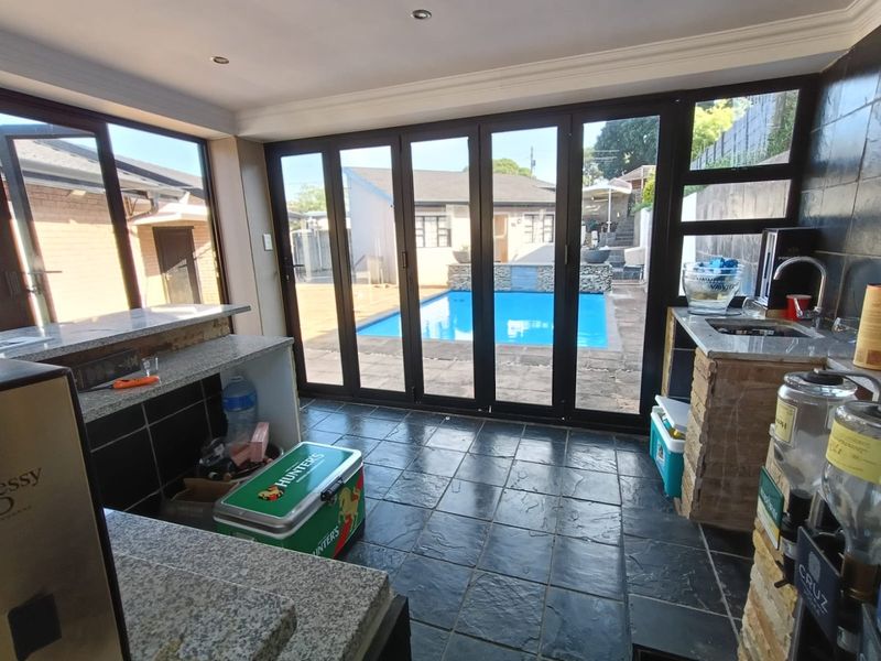 An indoor entertainment area featuring a built-in bar with granite countertops, stone flooring, and large bi-fold doors opening directly onto the pool area.