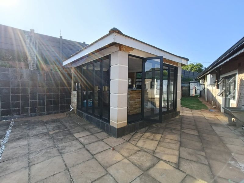 A detached outdoor entertainment structure featuring aluminum stacker doors, a built-in bar, and a paved patio area in the rear garden.