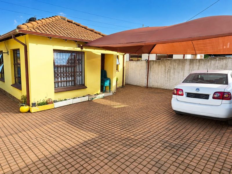 Front exterior view of a house featuring a paved driveway, a shade sail carport, and secure window bars.