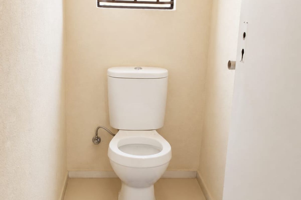 A compact guest toilet featuring tiled flooring, a standard white toilet suite, and a window fitted with security bars.