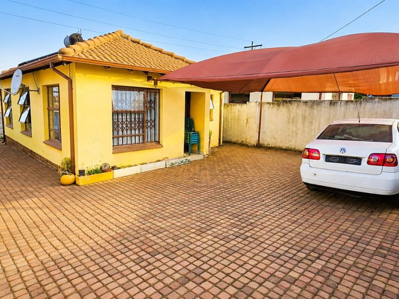 Front exterior view of a house featuring a paved driveway, a shade sail carport, and secure boundary walls.