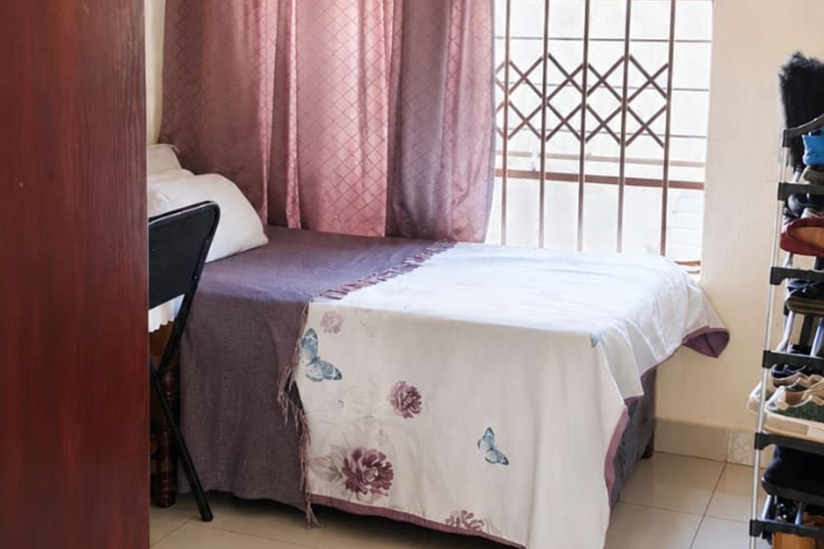 A compact bedroom featuring tiled flooring and a window fitted with a security gate, providing functional living space.