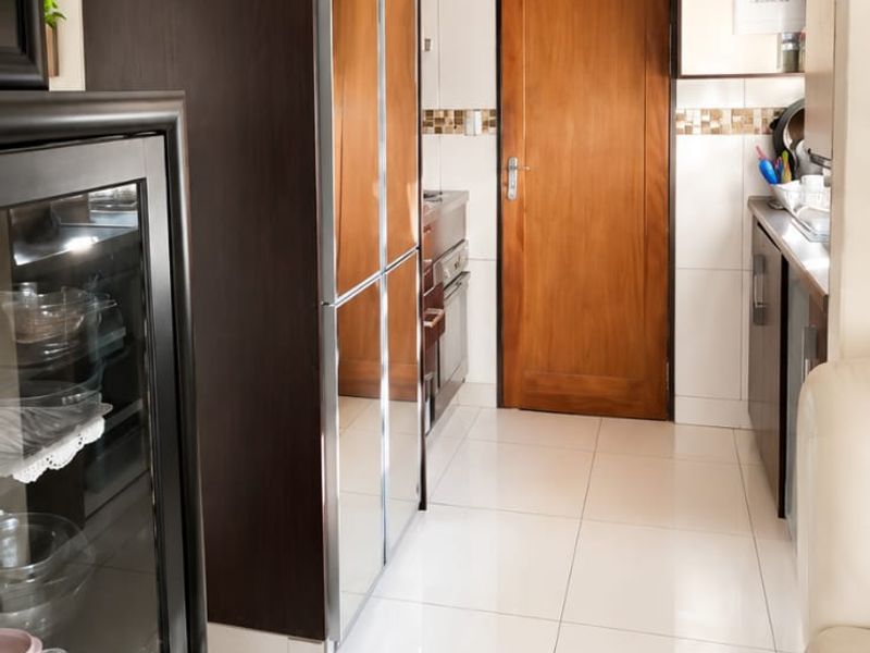 A functional kitchen featuring dark built-in cabinetry, light tiled flooring, and a tiled backsplash, leading to a solid wood door.