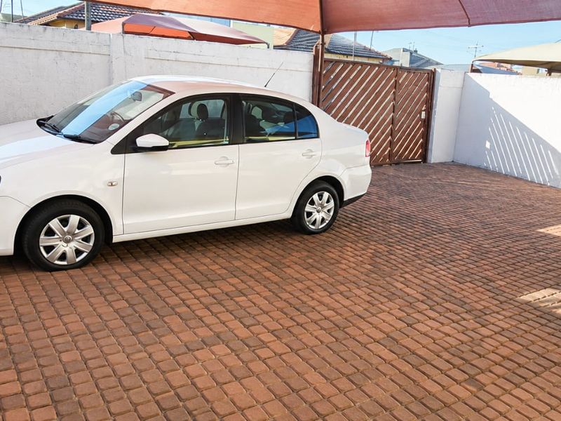 A paved outdoor parking area featuring a perimeter wall, security gate, and overhead shade sail for vehicle protection.