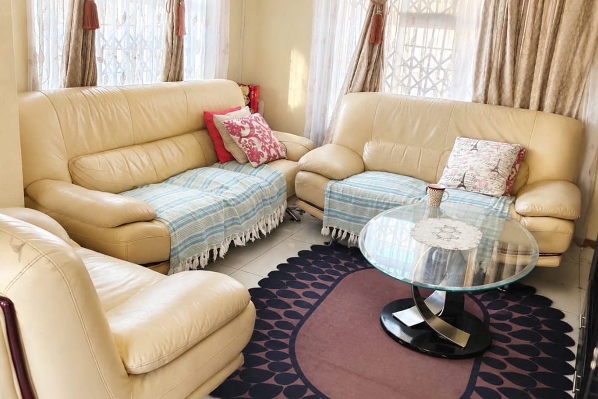 A comfortable living room featuring tiled flooring and natural light through large windows with security gates.